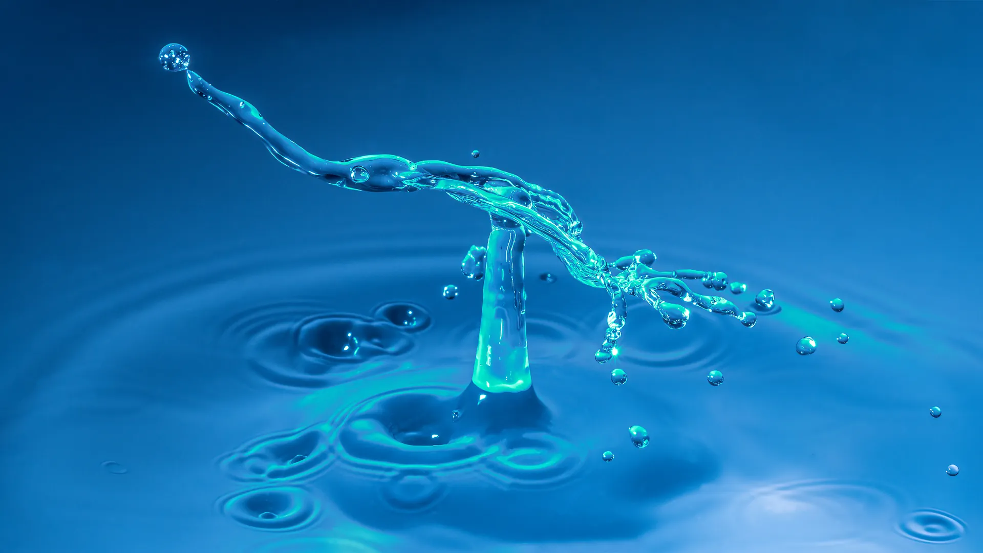 Ein türkiser Wasserstrahl mit nachfolgendem Einzeltropfen.
